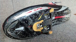 Road cleats are large and project from the sole of the shoe. Carbon fiber enables a very stiff foot-bed.
